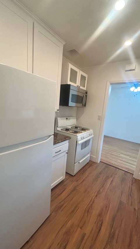 A kitchen with white appliances and wooden floors.
