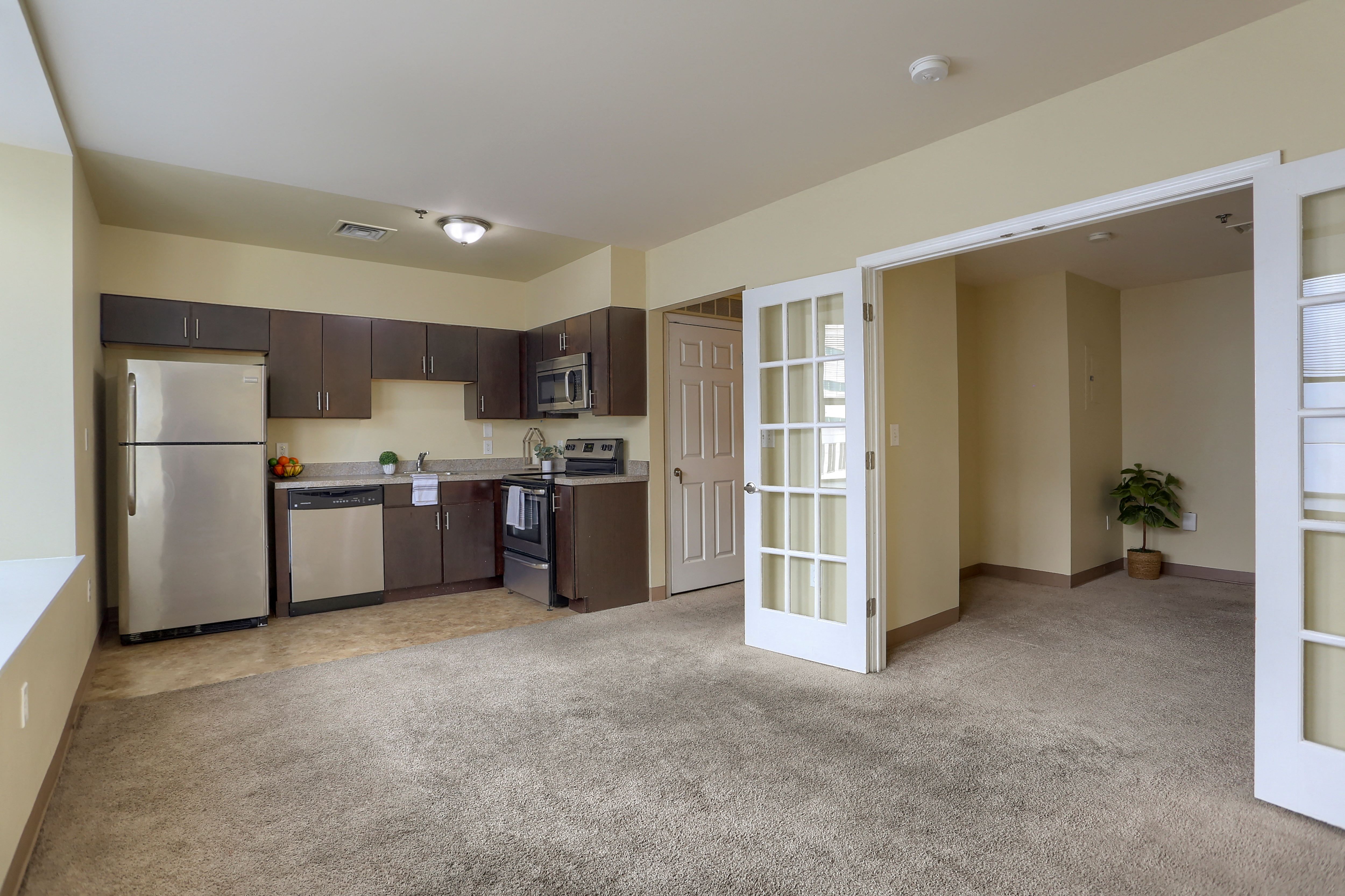 an empty living room with a kitchen with stainless steel appliances