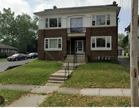 A two-story brick house with a car parked in front.