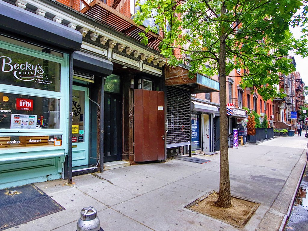 a tree on a sidewalk in front of shops on a city street