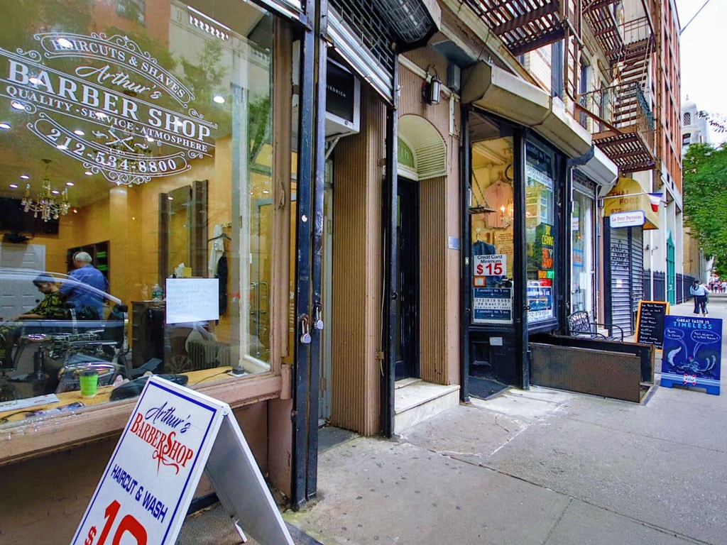 a sign outside of a barber shop on the sidewalk