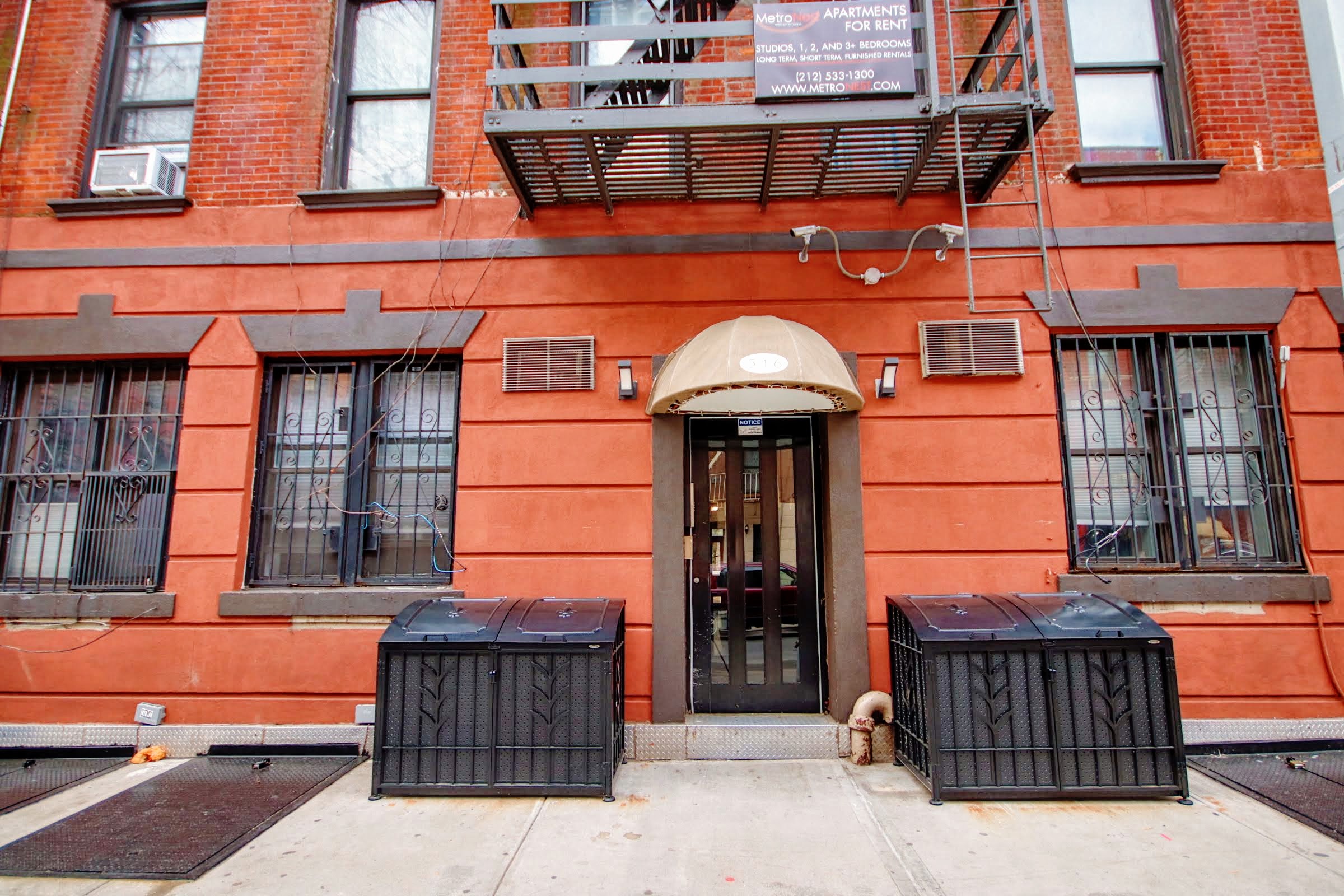the front of a brick building with a door and two dumpsters