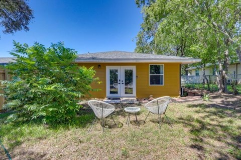 A yellow house with a white door and two chairs in front.