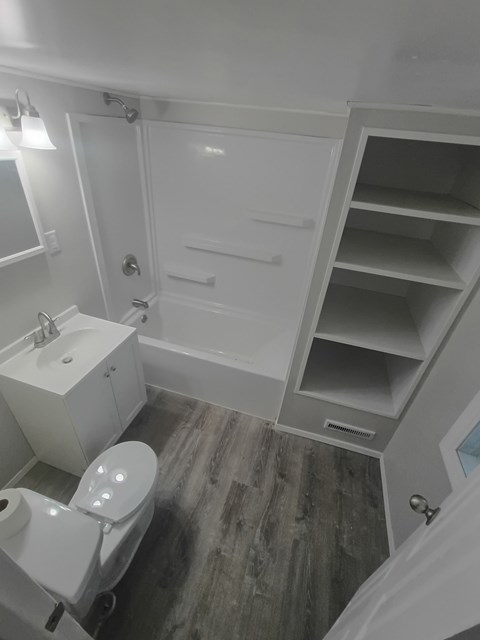 A white bathroom with a toilet, sink, and open cabinet.