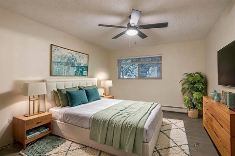 A bedroom with a bed, a ceiling fan, and a painting on the wall.