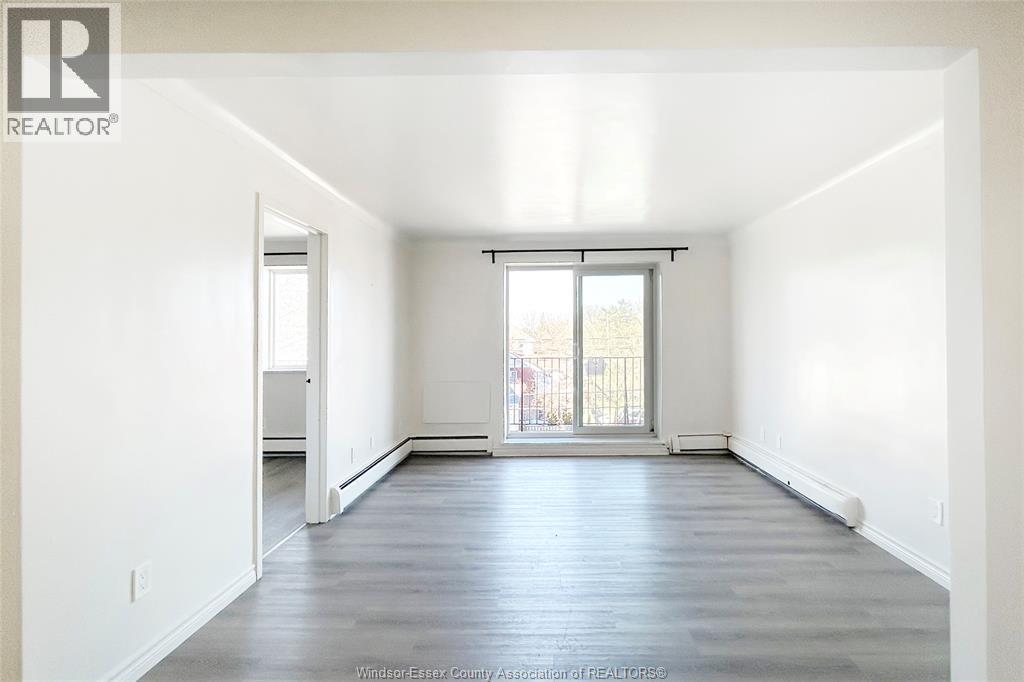 A spacious empty room with a large window and wooden flooring.