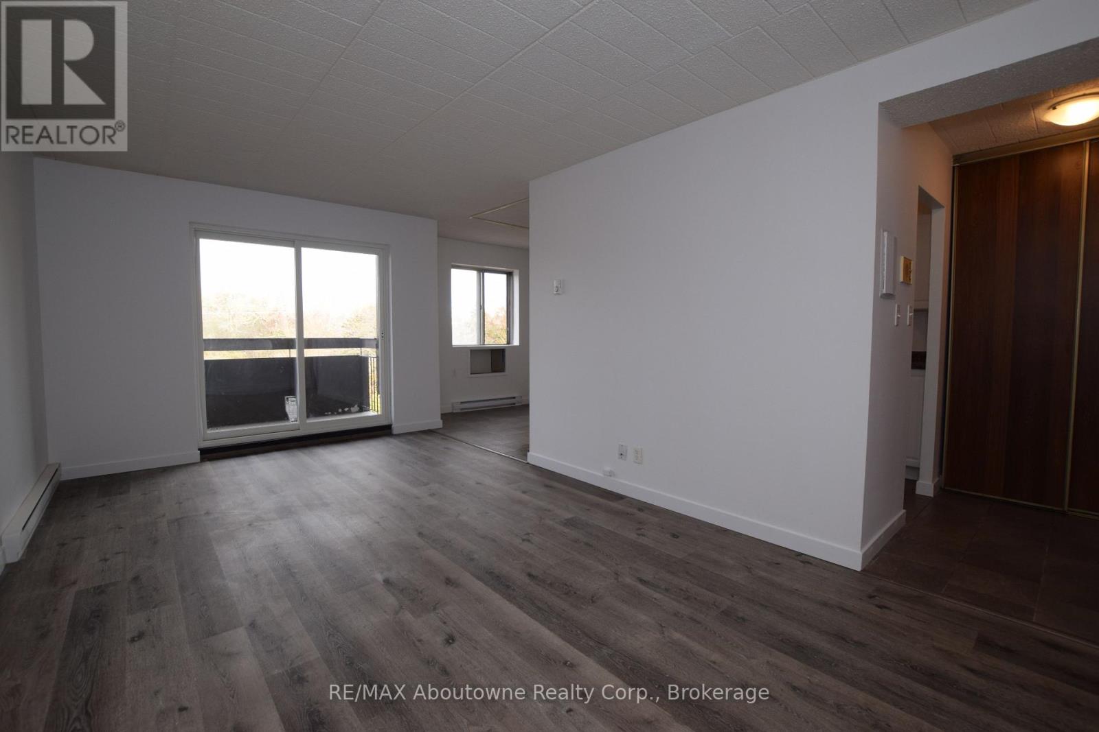 A spacious room with wooden flooring and white walls, with a large window providing a view of the outdoors.