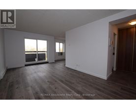A spacious room with wooden flooring and white walls, with a large window providing a view of the outdoors.
