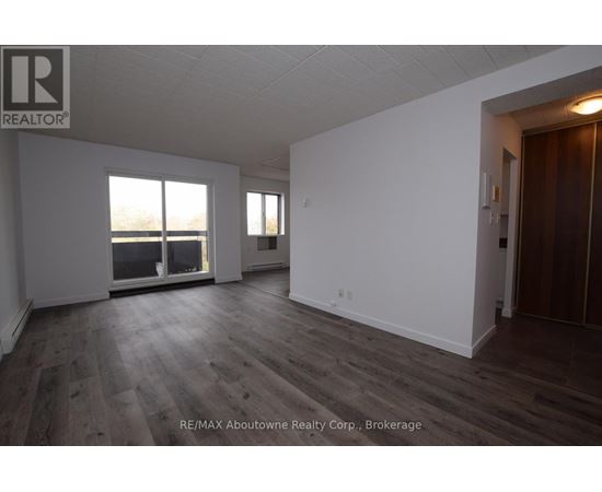 A spacious room with wooden flooring and white walls, with a large window providing a view of the outdoors.