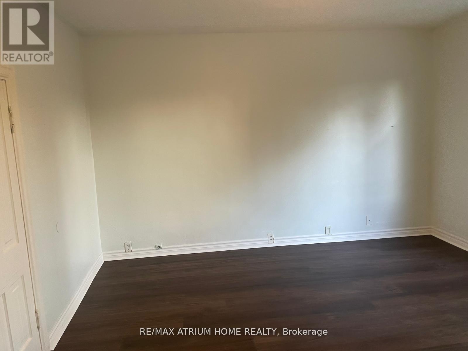 A room with wooden flooring and white walls, with a door on the left side.