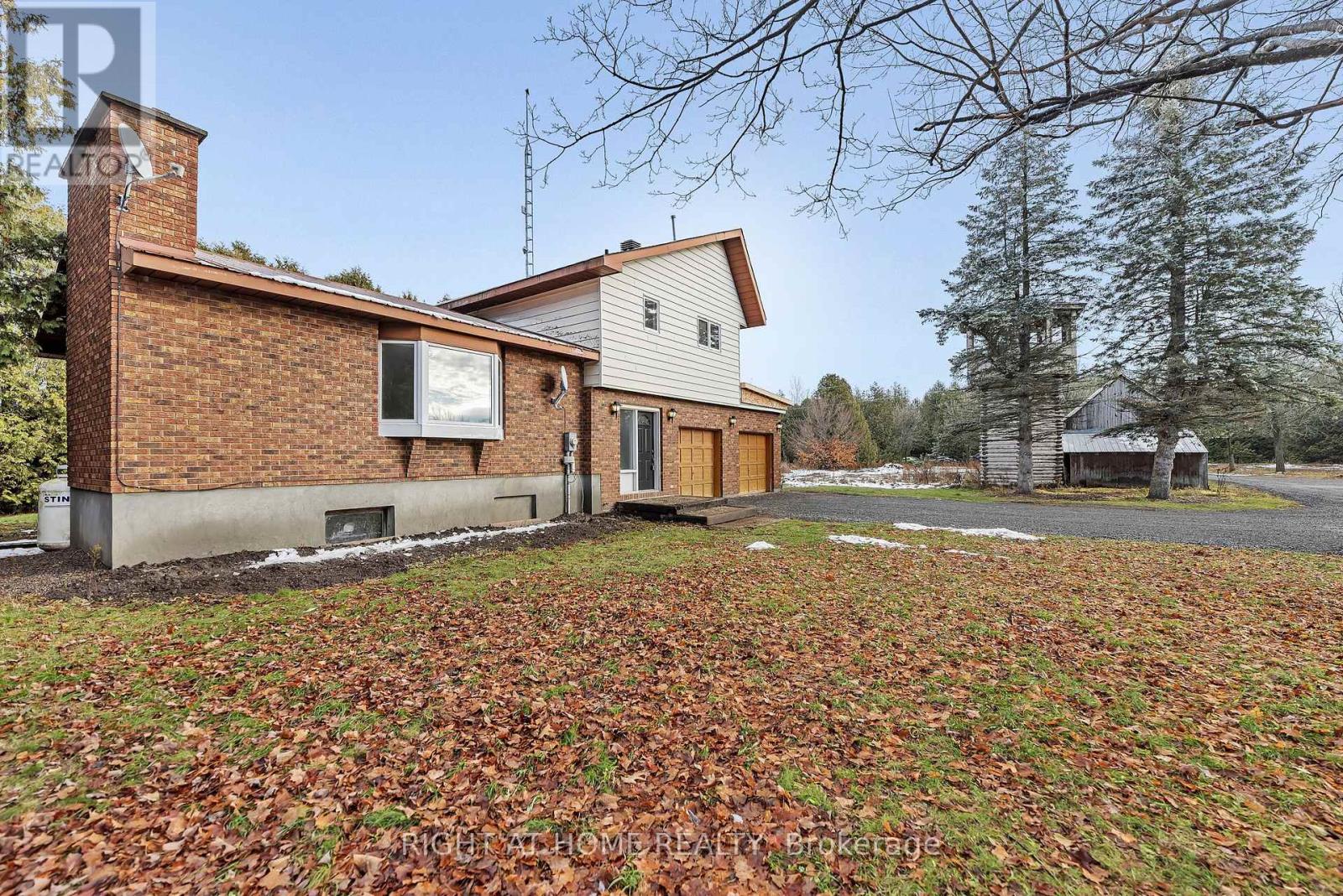 A house with a brown brick chimney and a white garage door is surrounded by a grassy area with fallen leaves.