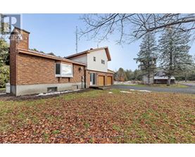 A house with a brown brick chimney and a white garage door is surrounded by a grassy area with fallen leaves.