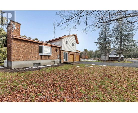 A house with a brown brick chimney and a white garage door is surrounded by a grassy area with fallen leaves.