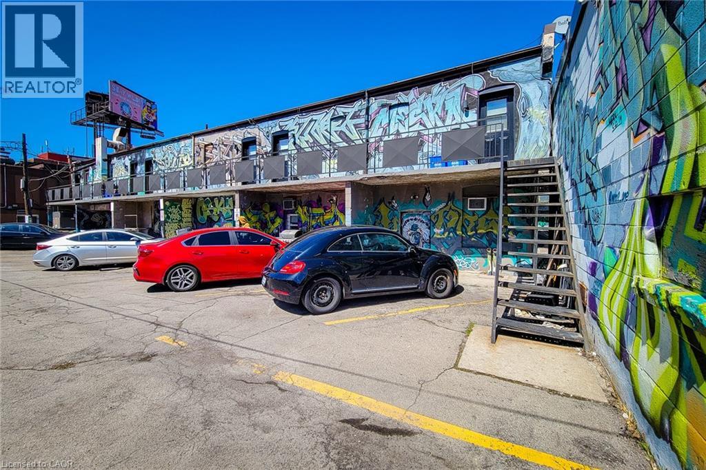 Three cars parked in a lot in front of a graffiti covered wall.