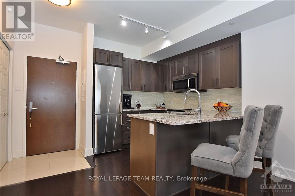 A kitchen with a refrigerator, microwave, and a counter with a chair.