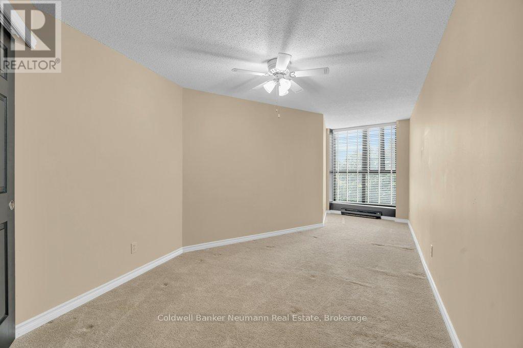 A spacious room with beige walls and carpeting, featuring a ceiling fan and a window with blinds.
