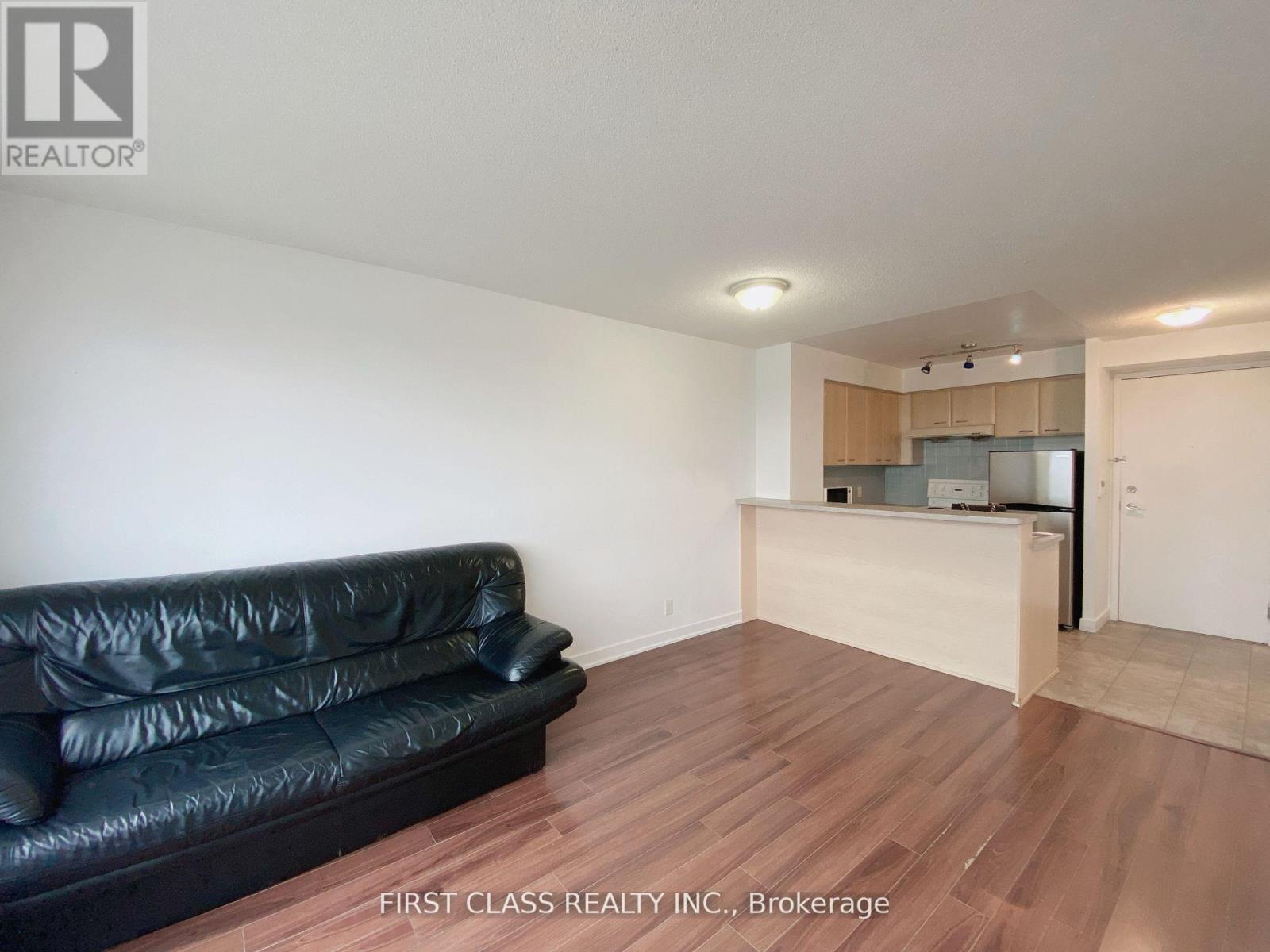 A black leather couch sits in a room with wooden floors and white walls.