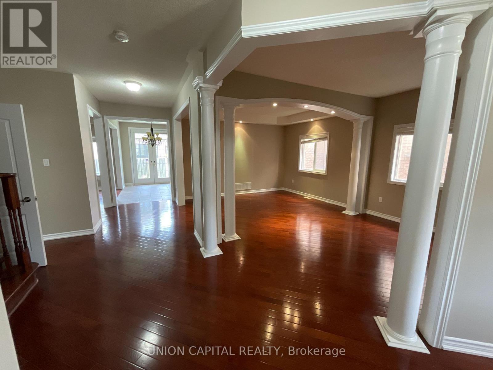 A spacious room with wooden floors and white columns.