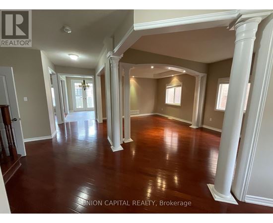 A spacious room with wooden floors and white columns.