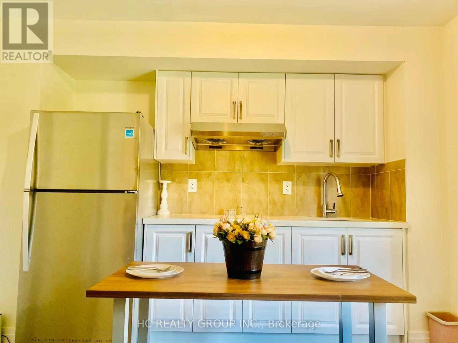 A kitchen with a refrigerator, wooden table, and a vase of flowers.