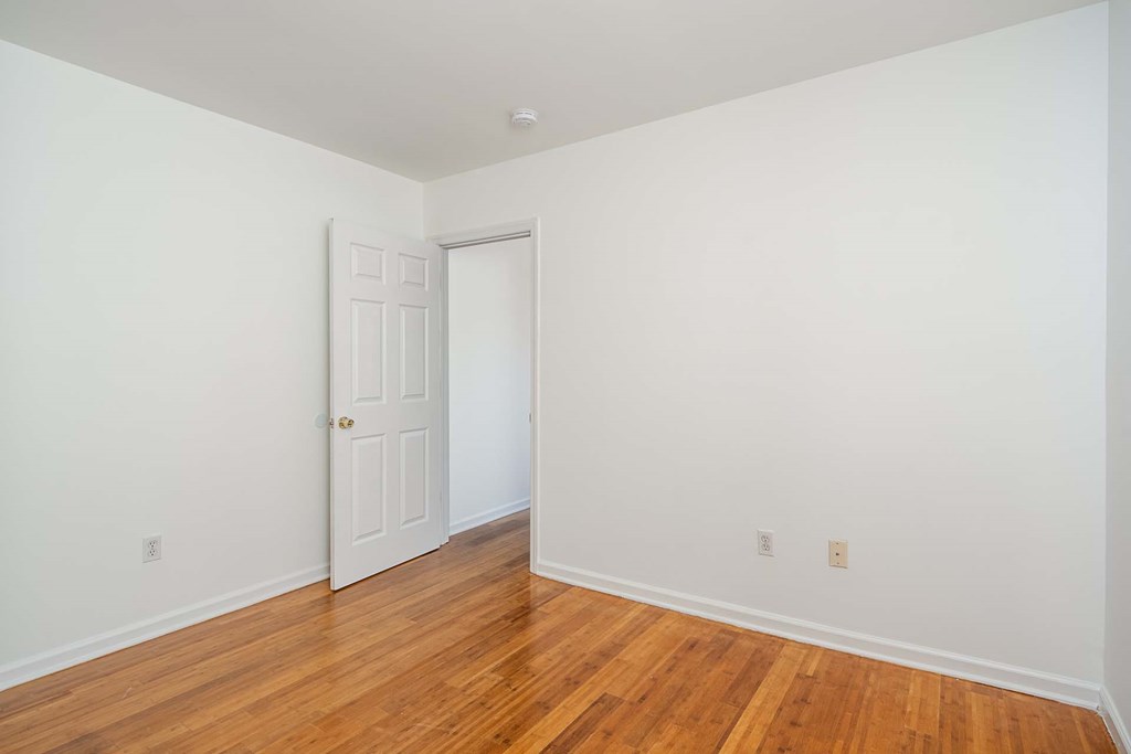 a bedroom with white walls and wood floors and a white door