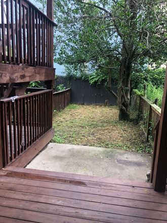 the backyard has a deck with a tree and a fence