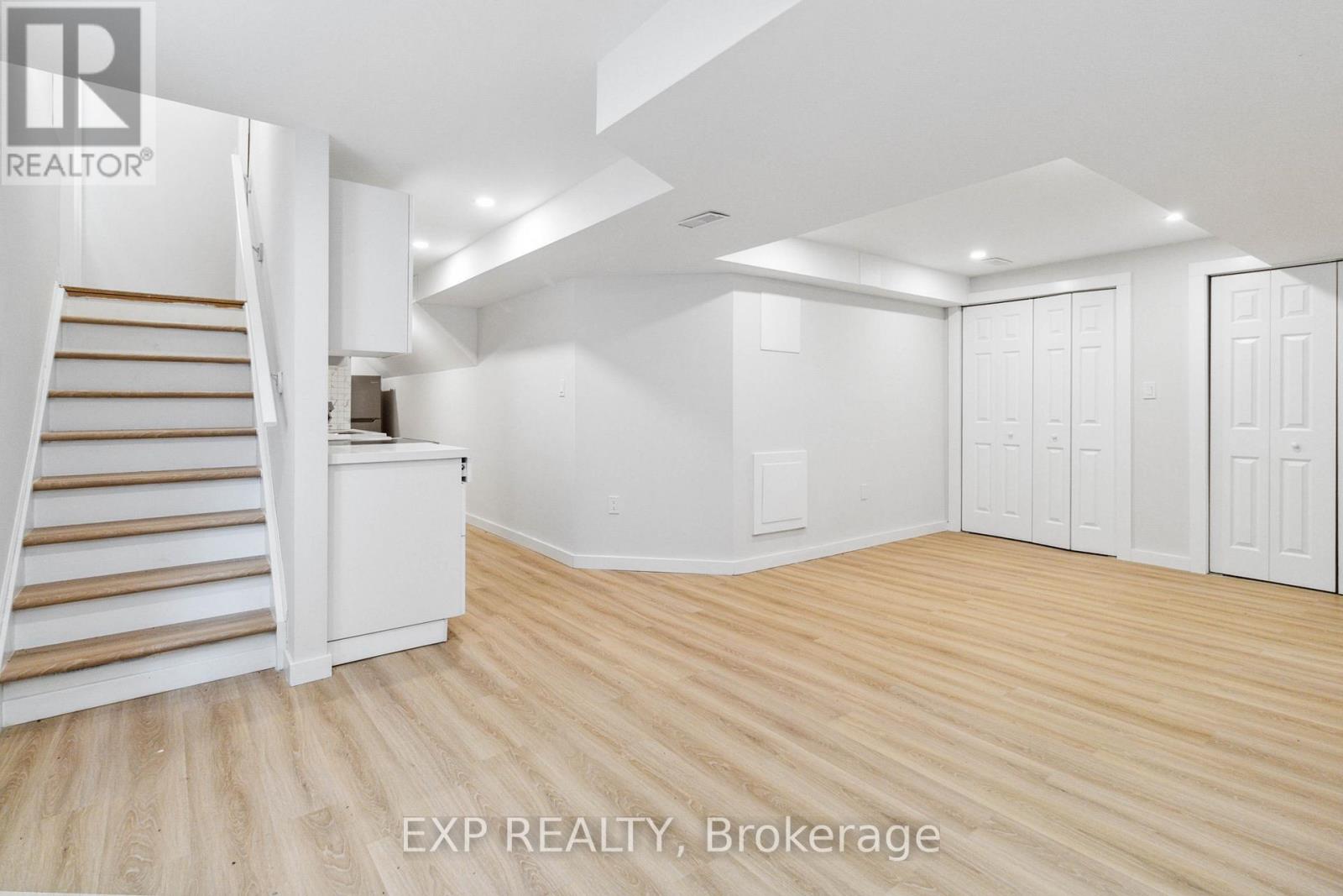A room with wooden floors and white walls, with a staircase on the left side.