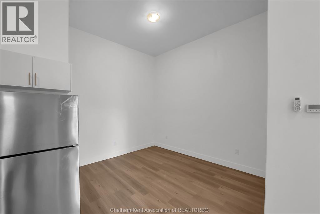 A white wall with a wooden floor and a refrigerator on the left.