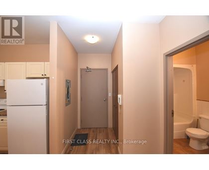 A hallway with a toilet and a sink visible through the door.