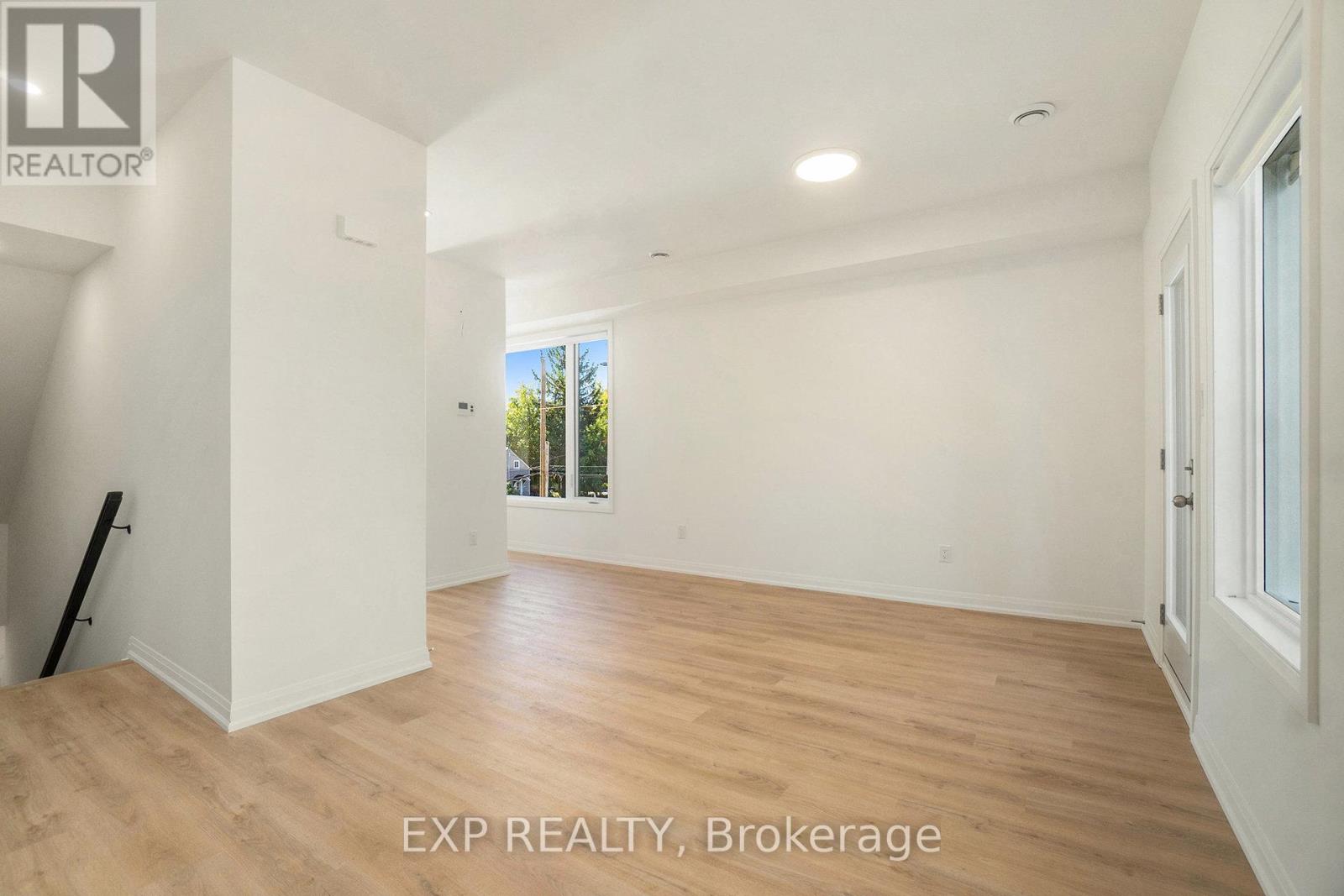 A room with wooden flooring and white walls, with a window showing trees outside.