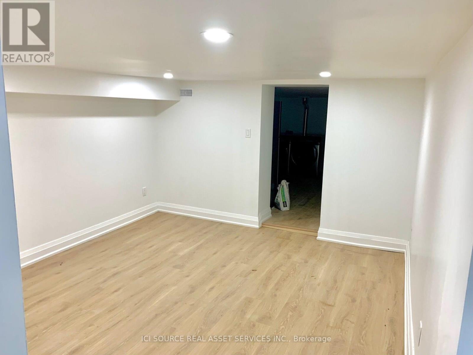 A room with wooden flooring and white walls, with a doorway leading to another room.
