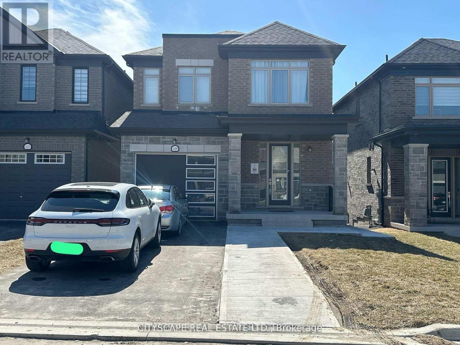 A white car is parked in front of a house with a realtor sign.