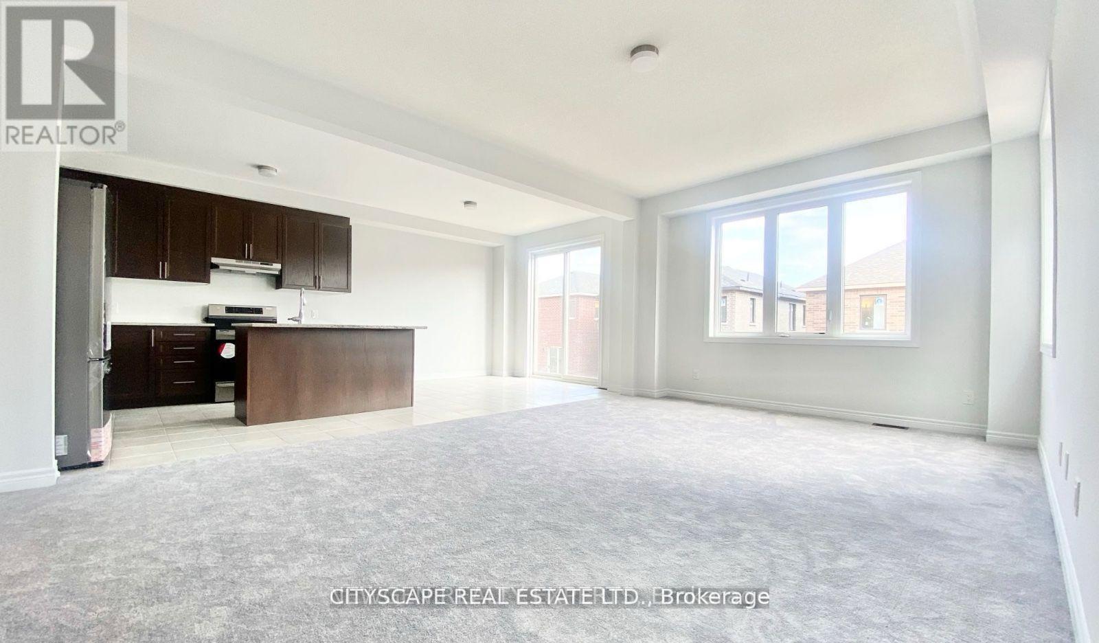 A spacious, empty room with a kitchen area to the left and a large window on the right wall.