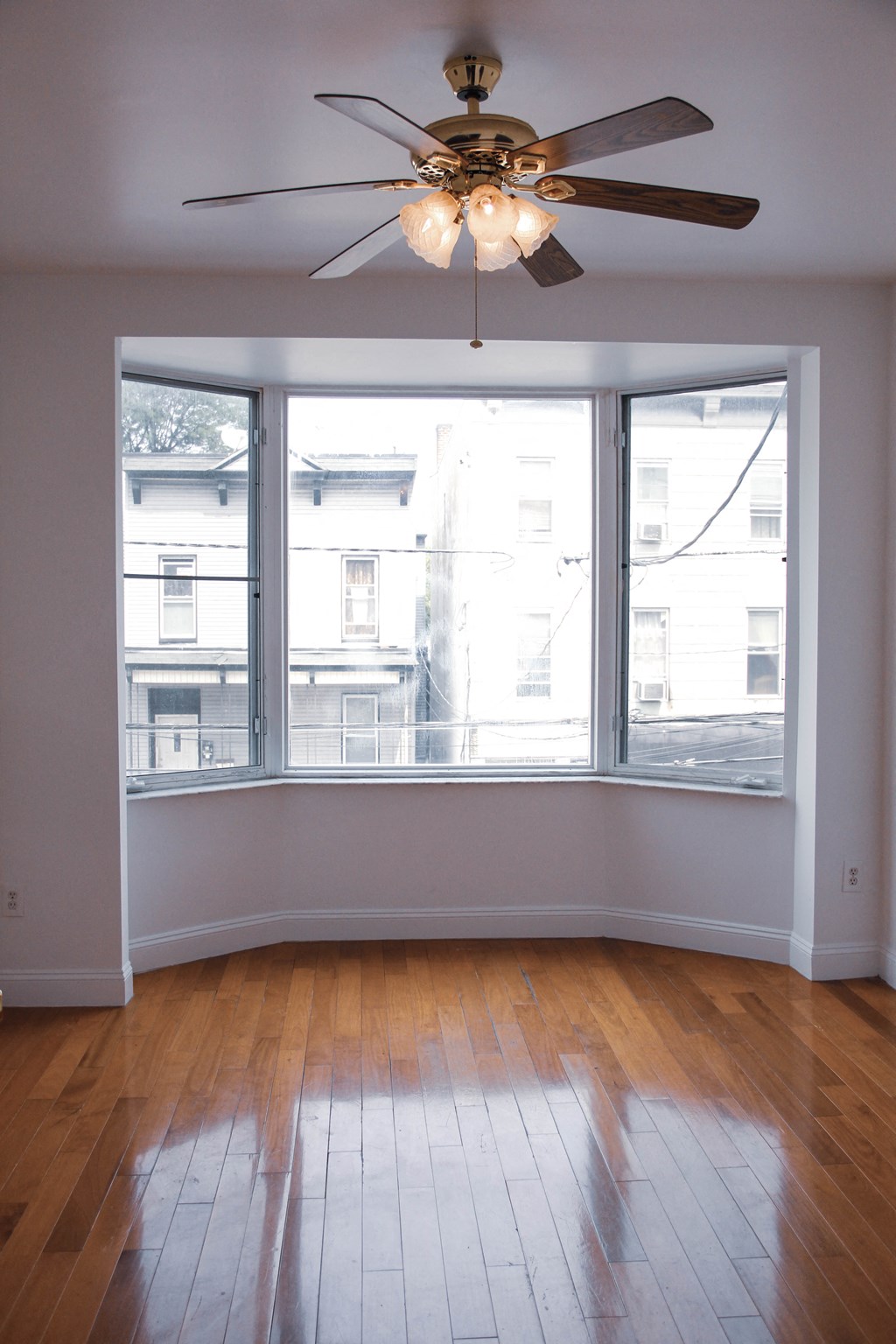 an empty living room with a large window and a ceiling fan