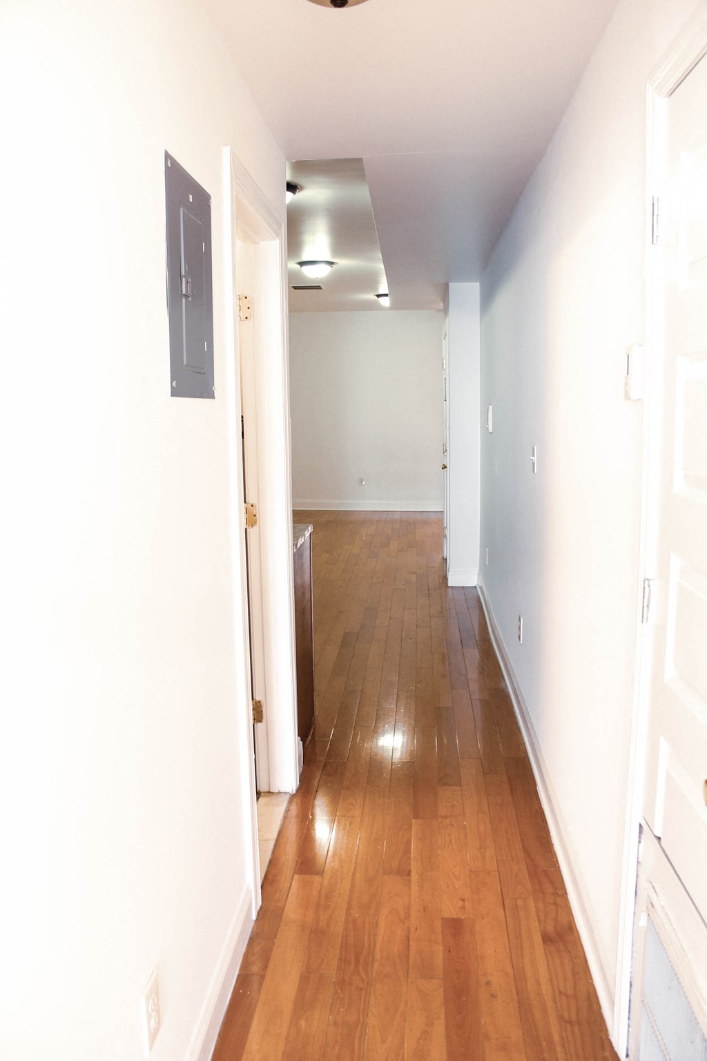 a hallway with wood floors and white walls and a door open