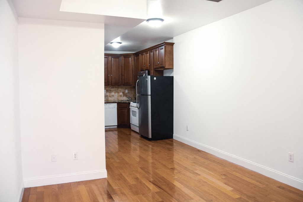 an empty living room and kitchen with wood floors and a refrigerator