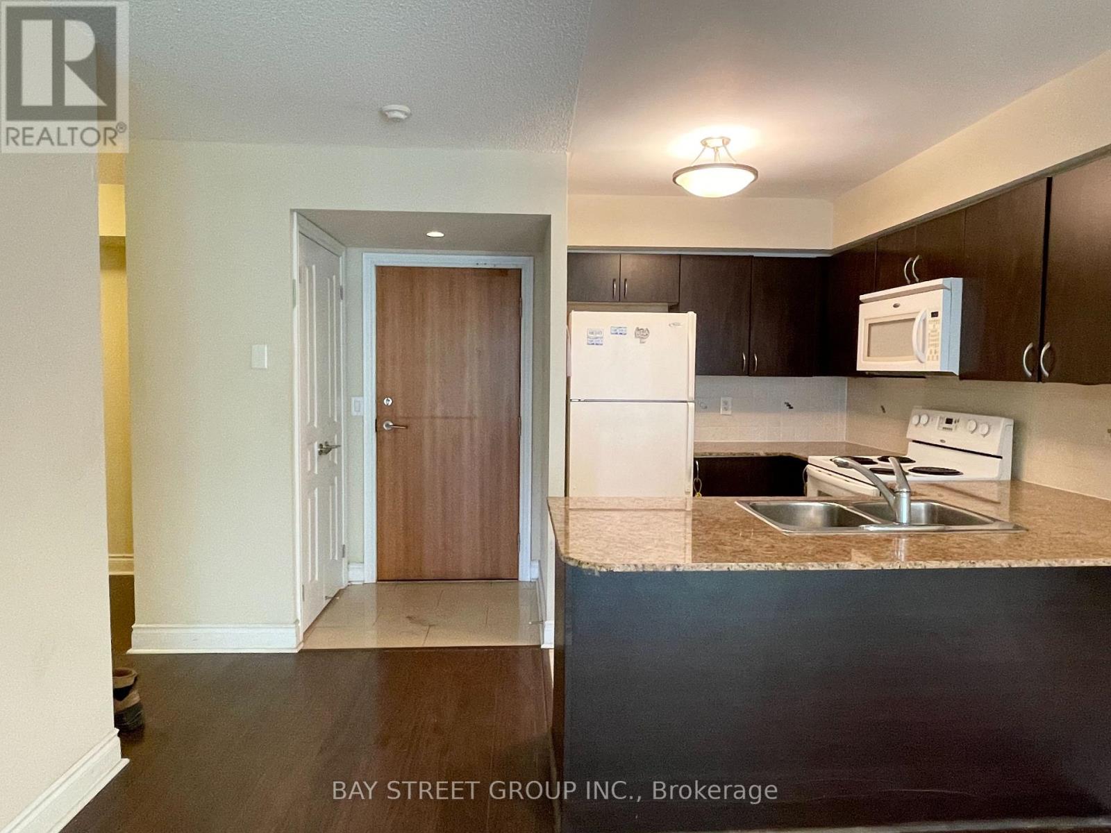 A kitchen with a white fridge and microwave, and a hallway with a wooden door.
