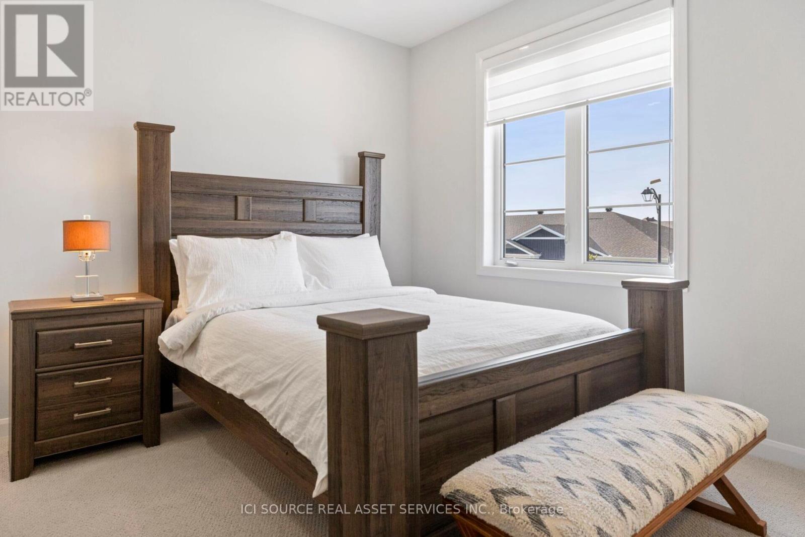 A bedroom with a large bed, a nightstand with a lamp, and a bench in front of the bed.