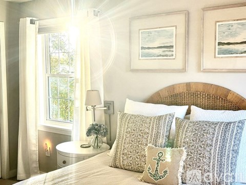 A bedroom with a bed, pillows, a nightstand with a lamp, and pictures on the wall.