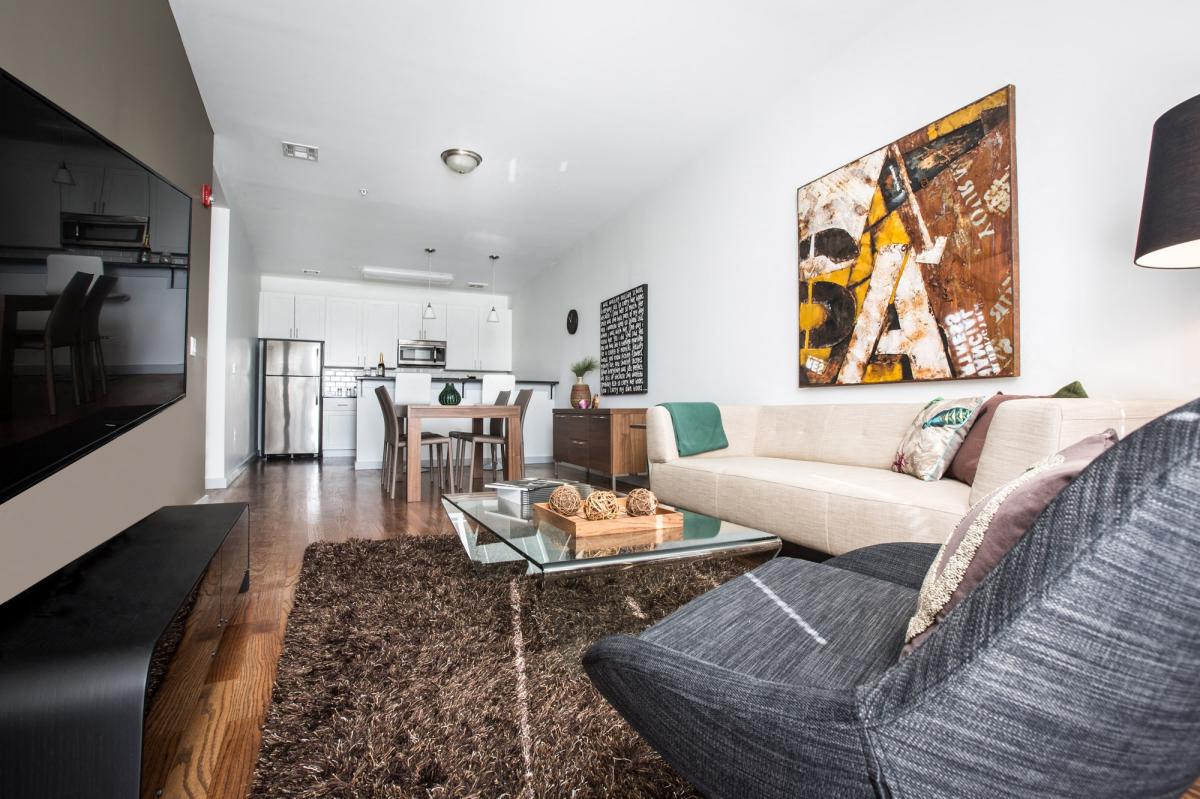 Model unit living room with brown rug, glass coffee table and white & gray couches