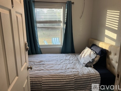 A bedroom with a bed, a window with blue curtains, and a white door.
