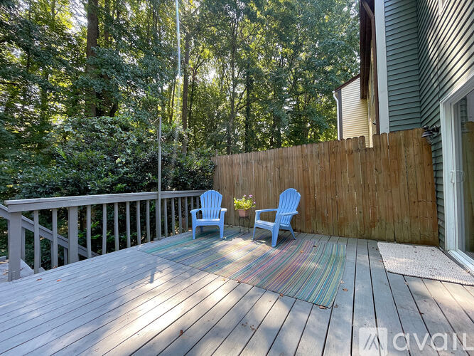 A deck with two chairs and a table is surrounded by a wooden fence and trees.