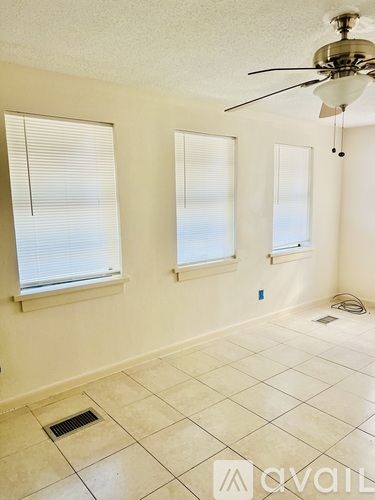 A room with a fan, two windows and a wall socket.