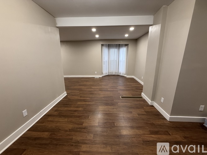 A spacious room with wooden flooring and a window with curtains.