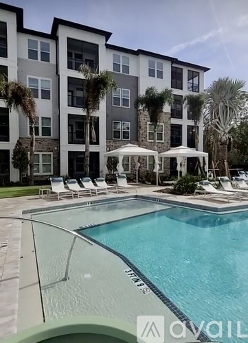 A swimming pool in front of a multi-story apartment building with outdoor lounge chairs and umbrellas.