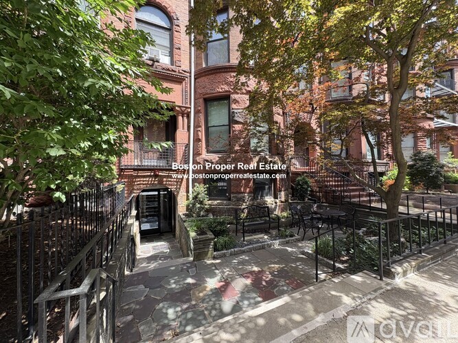 A building with a sign that says "Boston Proper Real Estate" is surrounded by trees and a metal fence.
