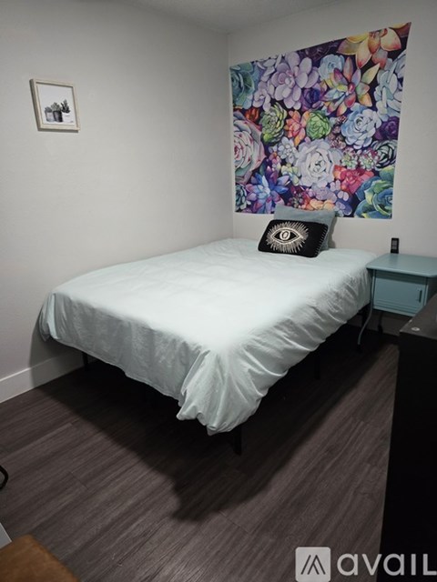 A bedroom with a white bed and a floral tapestry on the wall.