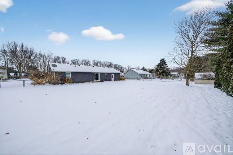 A snow-covered field with a house and trees in the background.