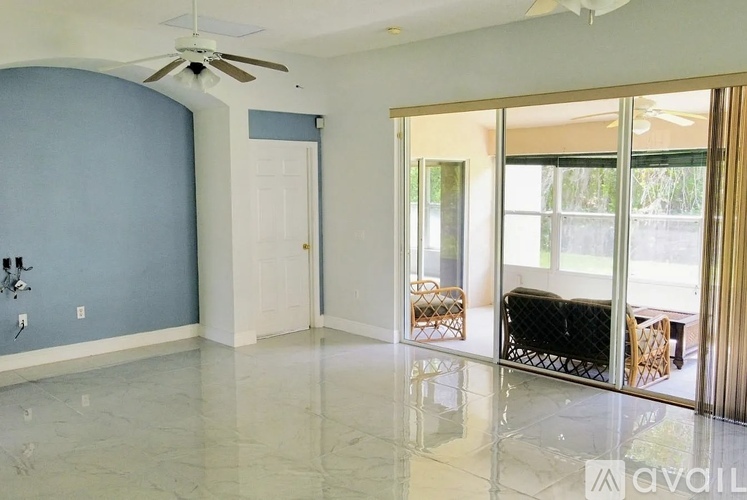 A spacious room with a ceiling fan and sliding glass doors leading to a balcony.