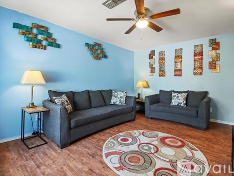 A living room with a grey couch, a grey armchair, a round rug and a ceiling fan.